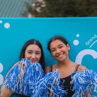 two students with pom poms posing in front of CAB backdrop at Laker Kickoff photo booth